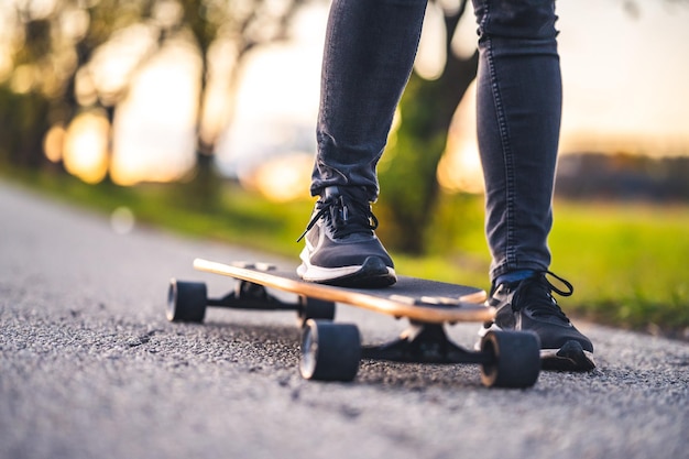 Kobieta jeździ po prostej drodze na longboardzie o zachodzie słońca Łyżwiarka w stroju casualowym trenująca na pokładzie podczas wieczornego zachodu słońca z pomarańczowym światłem Dziewczyna trzyma w dłoniach longboard