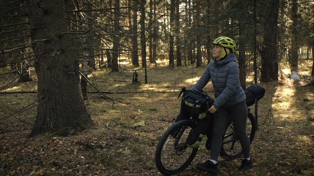 Kobieta jeździ po terenach mieszanych na rowerach turystycznych z bikepackingiem. Podróż podróżnika z torbami rowerowymi. Magiczny park leśny.