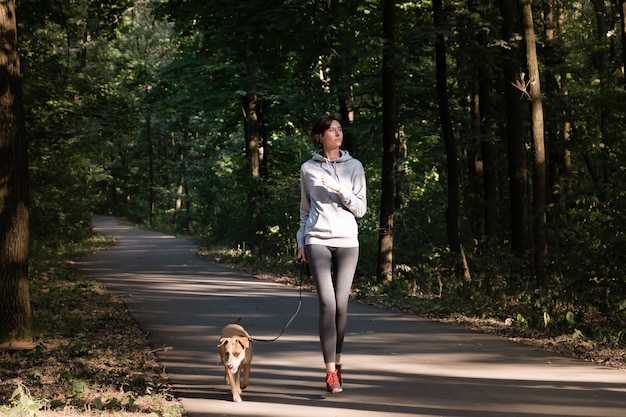 Kobieta joggingu z psem w pięknym lesie. Młoda kobieta ze zwierzęciem robi ćwiczenia biegowe biegowe na świeżym powietrzu.