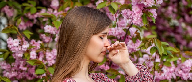Zdjęcie kobieta kicha w chusteczkę w pobliżu drzewa pełnego kwiatów.