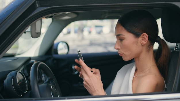 Kobieta kierowca patrząca na ekran telefonu siedząca na kołach samochodu bliska kobieta z telefonem