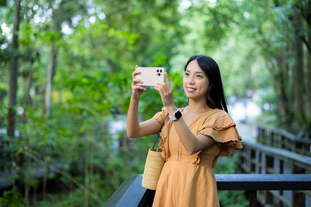 Kobieta korzysta z telefonu komórkowego, by zrobić zdjęcie w parku.