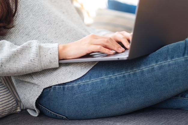 Kobieta korzystająca z laptopa i pracująca na nim, siedząc na kanapie w domu