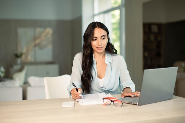 Kobieta korzystająca z laptopa i robiąca notatki w domu w biurze