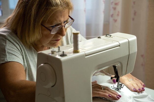 Kobieta krawcowa w okularach koncentrująca się podczas szycia na maszynie do szycia