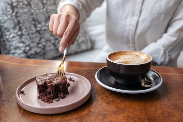 Kobieta Krojenia Ciasta Brownie Widelcem Z Filiżanką Kawy Na Drewnianym Stole W Kawiarni