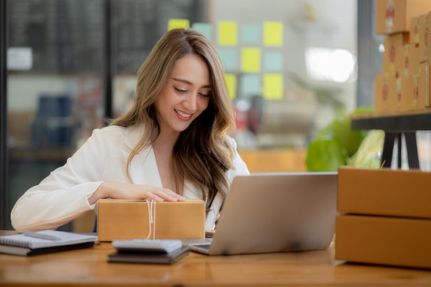 Kobieta, która prowadzi działalność e-commerce, pisze listę klientów na papierze przed wysłaniem do nich, prowadzi działalność e-commerce na stronach internetowych i w mediach społecznościowych Koncepcja sprzedaży produktów online