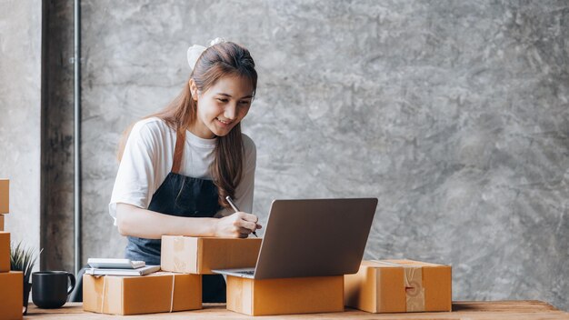 Kobieta, która prowadzi działalność e-commerce, pisze listę klientów na papierze przed wysłaniem do nich, prowadzi działalność e-commerce na stronach internetowych i w mediach społecznościowych Koncepcja sprzedaży produktów online