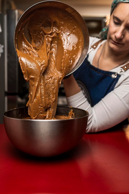 Kobieta kucharz wkłada świeżo zrobiony domowy dulce de leche z garnka do miski, aby przygotować domowy argentyński przepis alfajores