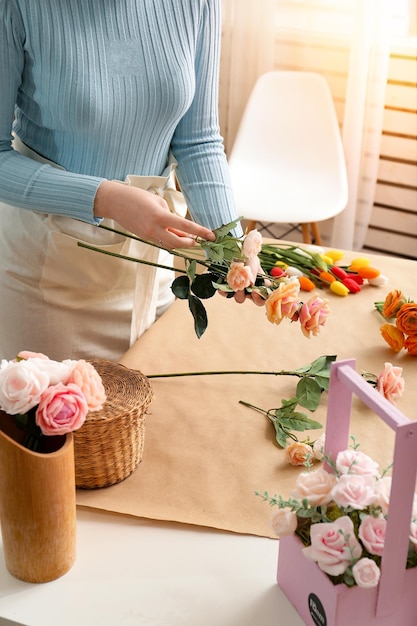 Kobieta kwiaciarnia robi bukiet pięknych wiosennych kwiatów przy jasnym drewnianym stole