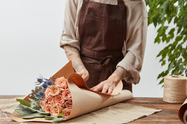 Kobieta kwiaciarnia zawija świeży bukiet róż w ozdobny papier na drewnianym stole na jasnej ścianie