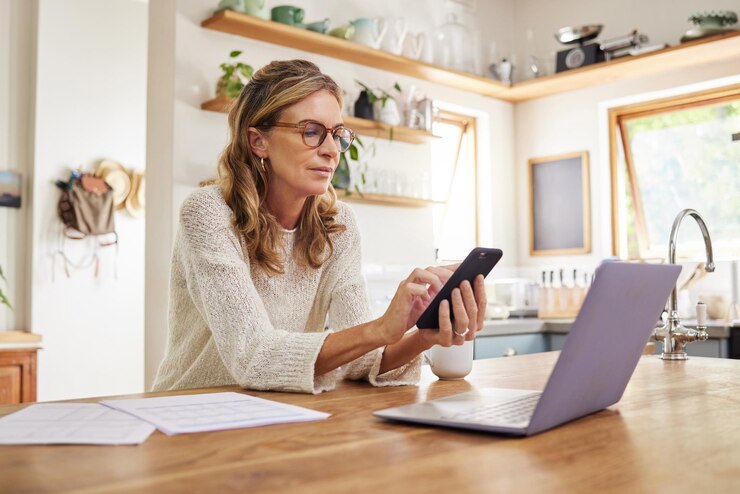 Kobieta laptop lub fintech aplikacja na telefon w domu lub domowej kuchni do finansów budżet inwestycje księgowość lub ubezpieczenie podatki Myśląca dojrzała osoba z papierem technologicznym lub dokumentem na pożyczkę emerytalną