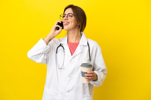 Kobieta lekarka na żółtym tle trzymająca kawę na wynos i telefon komórkowy