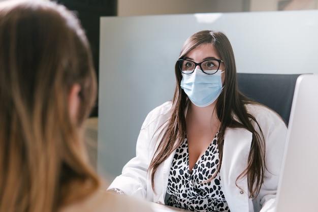 Kobieta lekarz noszenie maski i rozmawia z pacjentem w swoim biurze