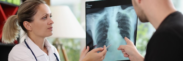 Kobieta lekarz pokazująca rentgen pacjentowi w gabinecie medycznym wyjaśniając uszkodzenie kręgosłupa kości