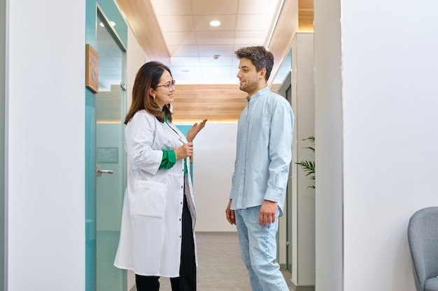 Kobieta lekarz rozmawia z pacjentem. Lekarz wyjaśniający coś młodemu mężczyźnie na korytarzu