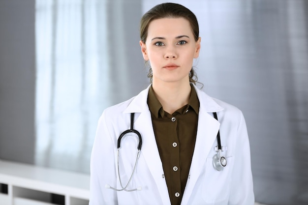 Kobieta lekarz szczęśliwa i wesoła stojąc w gabinecie szpitalnym Doskonała obsługa medyczna w klinice Koncepcja medycyny i opieki zdrowotnej