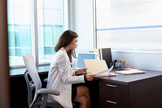 Kobieta lekarz ubrana w biały płaszcz, czytanie notatek w biurze