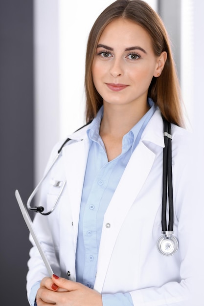 Zdjęcie kobieta lekarz używająca tabletu, stojąc prosto w pobliżu okna w szpitalu. szczęśliwy lekarz w pracy. koncepcja medycyny i opieki zdrowotnej.