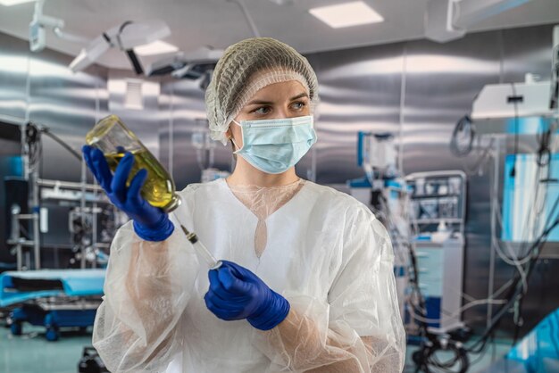 Kobieta lekarz w jednolitej masce na twarz w rękawiczkach przygotowuje strzykawkę z antybiotykiem w działaniu