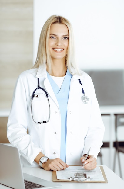 Zdjęcie kobieta lekarz w pracy w szpitalu podekscytowana i zadowolona ze swojego zawodu blondynka lekarz kontroluje zapisy historii leków i wyniki egzaminów podczas korzystania ze schowka pojęcie medycyny i opieki zdrowotnej