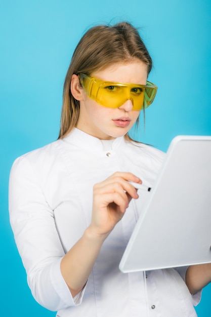 Kobieta lekarz w żółtych okularach i biurku na niebieskim tle