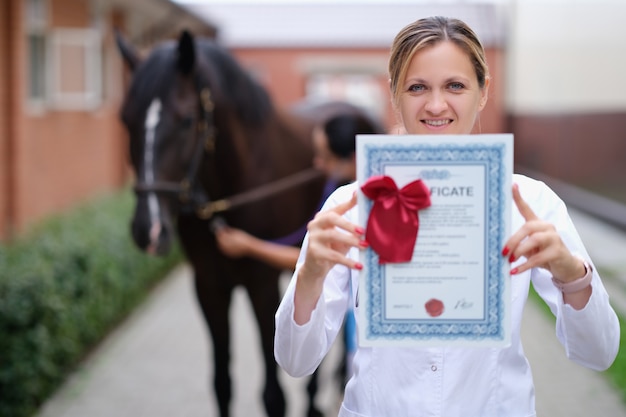 Zdjęcie kobieta lekarz weterynarii posiadający certyfikat szkolenia na tle konia
