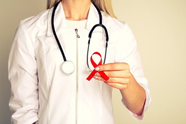 Kobieta lekarz z AID, czerwoną wstążką HIV. Koncepcja raka. Doktor trzyma czerwoną wstążkę, aby uświadomić sobie Światowy dzień AIDS 1 grudnia