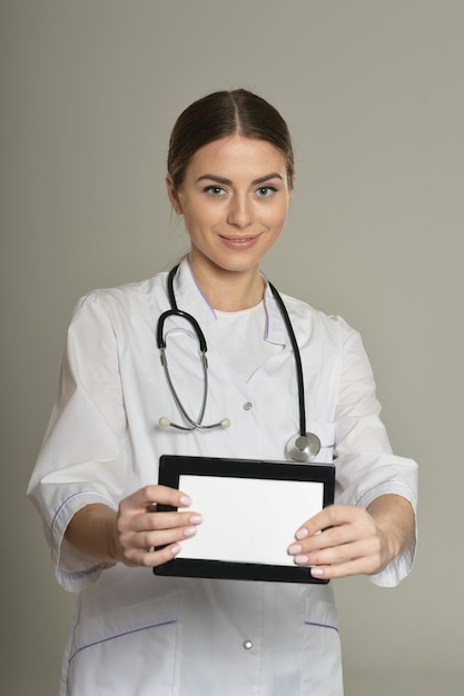 Kobieta lekarz z komputerem typu tablet, stojąc na szarym tle