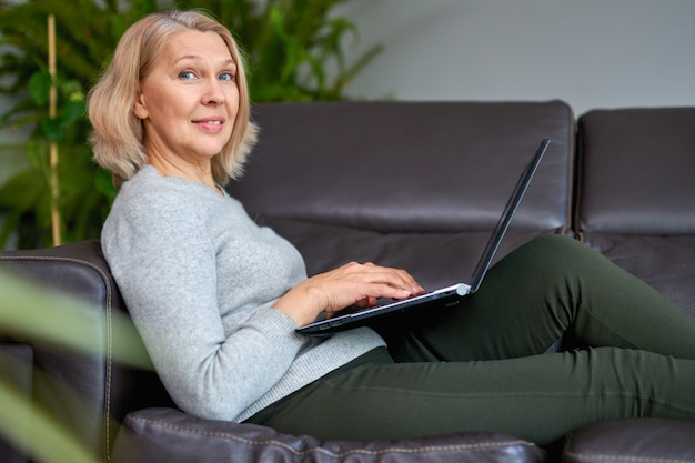 Kobieta, leżąc na kanapie w domu, koncentrując się, jak działa na laptopie.