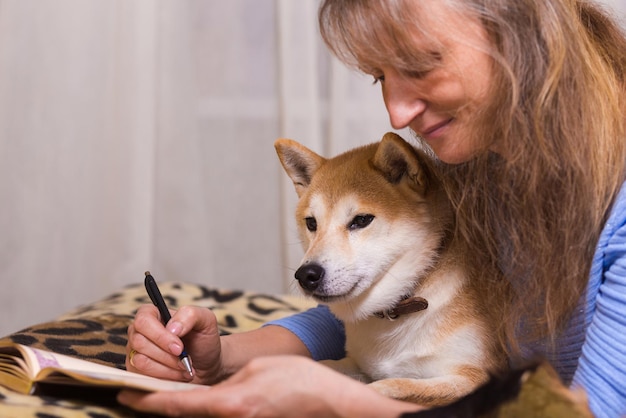 Kobieta Leżąca Na łóżku I Pisząca W Pamiętniku Ze Swoim Towarzyszem Shiba Inu Psem. Miłość, Wspólnota I Zwierzęta Domowe W Domu.