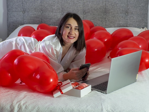 Kobieta leżąca na łóżku z czerwonymi balonami na przyjęcie walentynkowe