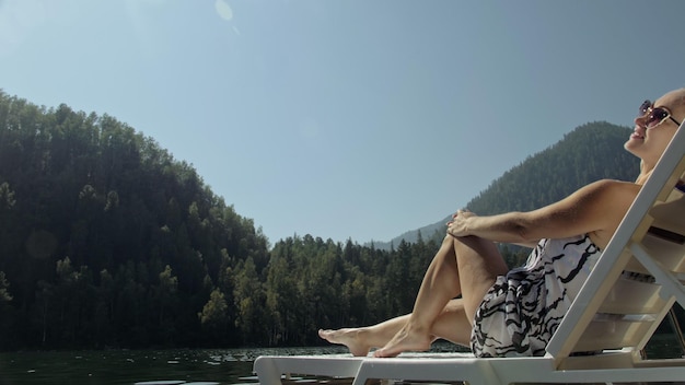 Kobieta leży na leżaku w okularach przeciwsłonecznych i jedwabnym szalu boho Dziewczyna odpoczywa na podwodnym molo z drewna