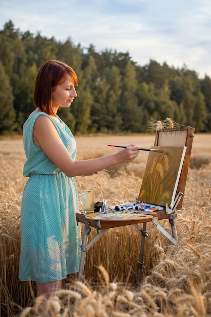 Zdjęcie kobieta malarka wykonująca swoją pracę na polu pszenicy młoda dziewczyna malująca kłoski pszenicy na zewnątrz