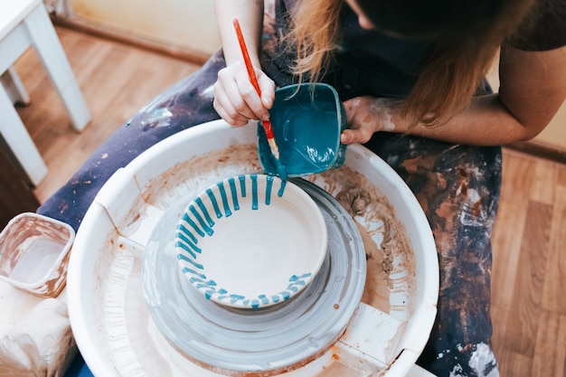 Kobieta maluje ceramiczny talerz pędzlem i niebieską farbą