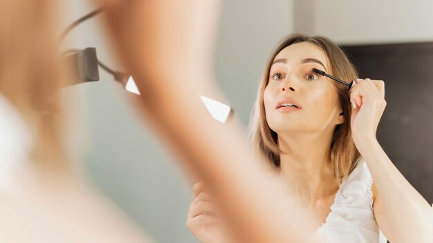 Kobieta maluje rzęsy patrząc w lustro w salonie kosmetycznym