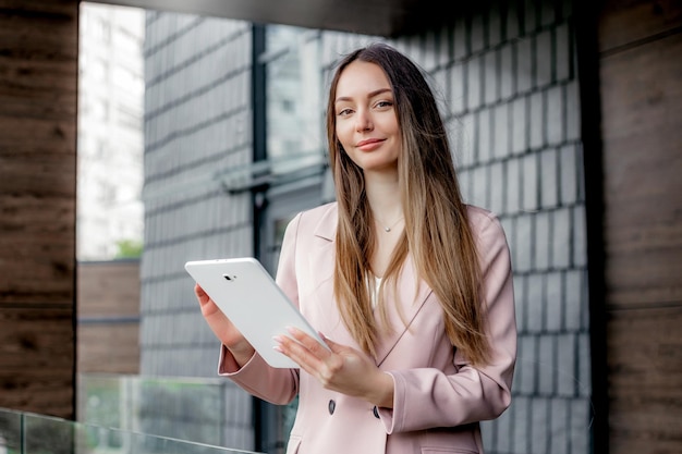 Kobieta marketerka w garniturze uśmiechająca się trzymająca tabletkę i patrząca w kamerę
