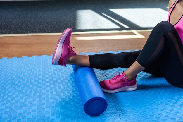 Kobieta masująca nogi wałkiem do masażu po ciężkim treningu na zajęciach fitness