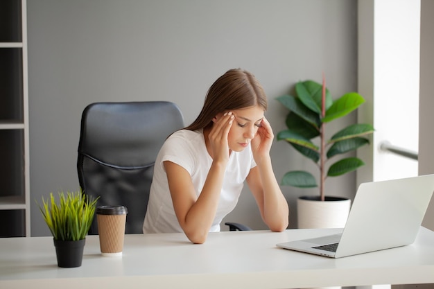 Kobieta masująca świątynie cierpiąca na ból głowy po pracy przy komputerze