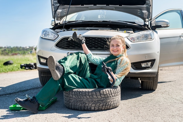 Kobieta mechanik siedzi na koło zapasowe przed samochodem