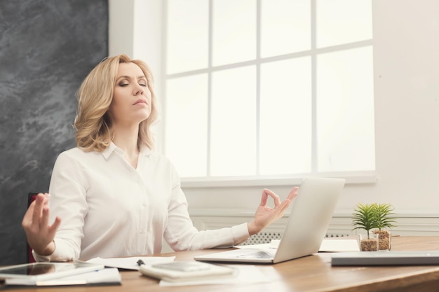 Zdjęcie kobieta medytuje w biurze. portret kobiety w średnim wieku w formalnym stroju uspokaja się w miejscu pracy, kopia przestrzeń