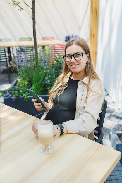 Kobieta menedżer siedzi na tarasie na świeżym powietrzu w kawiarni i pracuje online z kawą Kobieta freelancerka pracuje zdalnie online siedząc w letniej kawiarni Praca zdalna