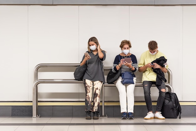 Kobieta, mężczyzna i starsza kobieta siedzący w metrze przestają patrzeć na swoje telefony komórkowe w masce