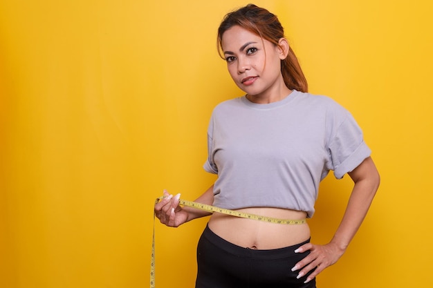 Kobieta mierząca talię za pomocą taśmy na żółtym tle Fitness and Sport Concept