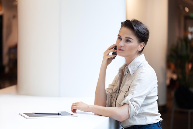 Kobieta mówi telefon w biurze. Piękna uśmiechnięta młoda kobieta.