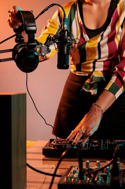 Kobieta muzyk używająca sprzętu dj i słuchawek do miksowania muzyki techno i odtwarzania remiksów elektrycznych na gramofonach, bawiąca się instrumentem stereo służącym do miksowania dźwięków, głośnością basów.
