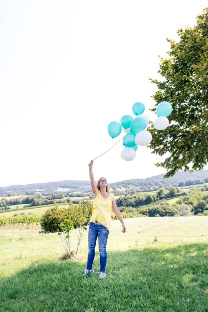 Zdjęcie kobieta na całej długości trzymająca balony na czyste niebo