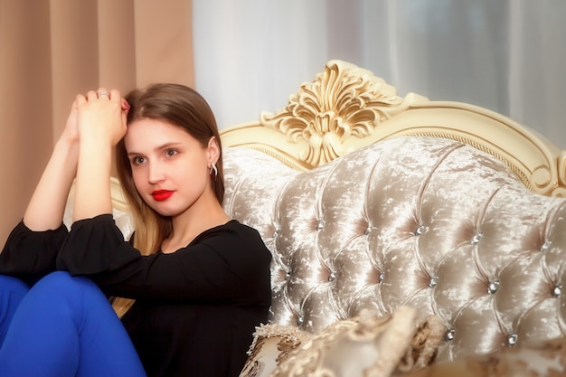Zdjęcie kobieta na kanapie pokoju hotelowego. ładna kobieta o słowiańskim wyglądzie w czarnej bluzce i niebieskich spodniach. szczęśliwa pani. spędź czas na wakacjach. śliczna dziewczyna się uśmiecha i pokazuje emocje