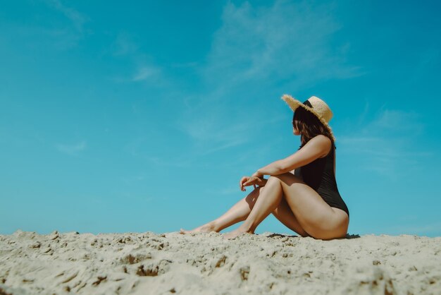 Kobieta na piaszczystej plaży w czarnym stroju kąpielowym, błękitne niebo na tle