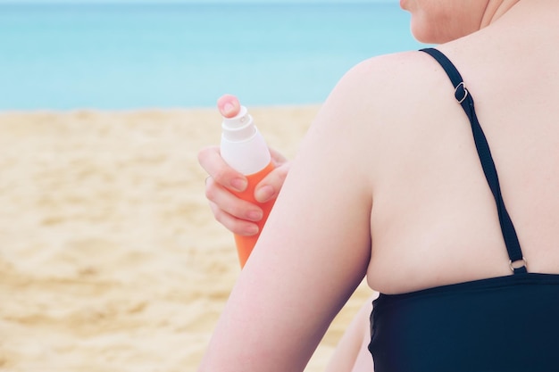 Kobieta na plaży nakłada krem przeciwsłoneczny na ręce z pomarańczowej butelki
